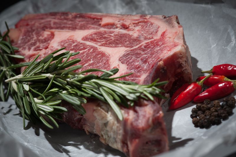 Ojo de bife crudo con grasa de cobertura sobre tabla de madera, mostrando la textura madurada